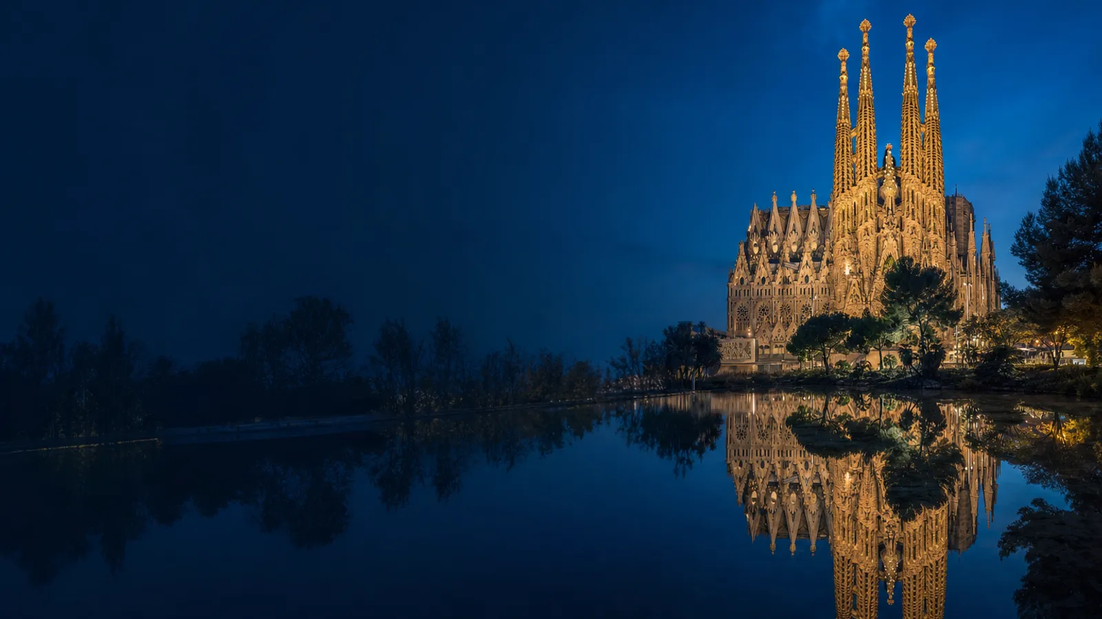 The Sagrada Família at blue hour, floodlit and reflected in the pond of Plaça de Gaudí