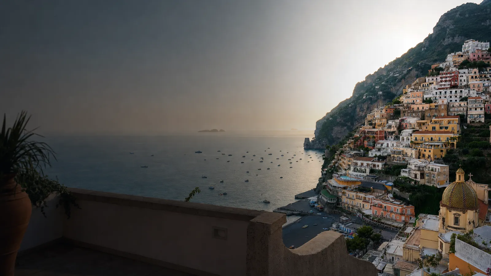 Terrace view over Positano's stacked pastel houses meeting the sea at golden hour