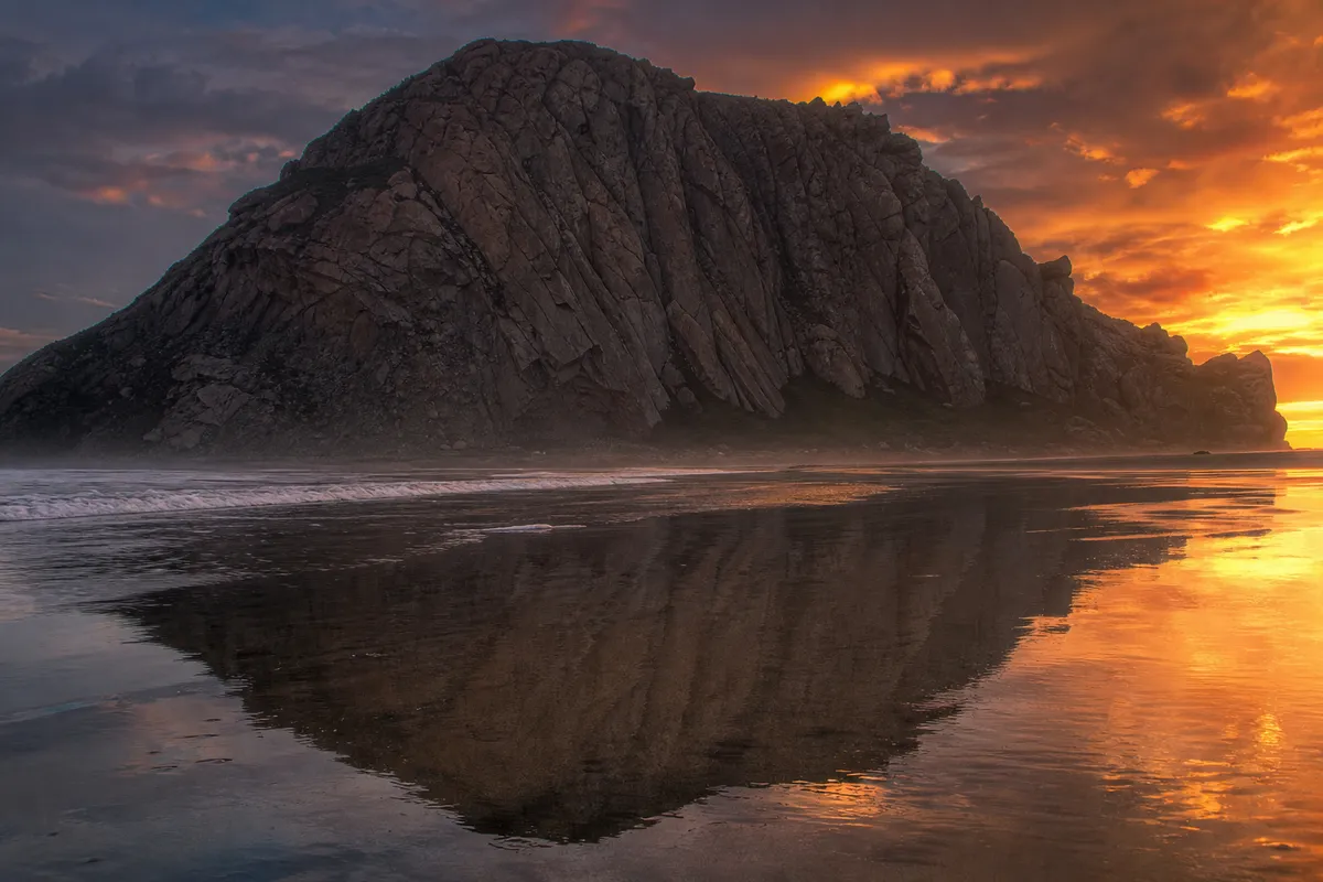 Morro Rock silhouetted at sunset across the wet sand, Morro Bay